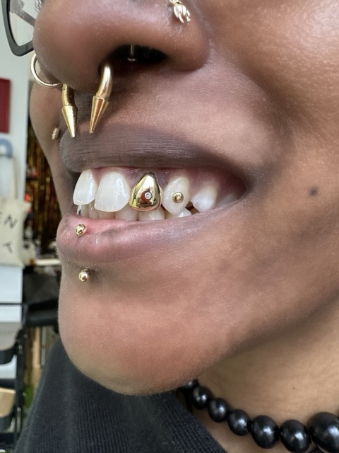 Tooth gems and a gold heart accent on the upper teeth, worn with spiked septum jewelry and a labret stud