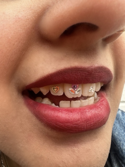 Close-up of colorful heart and flower tooth gems across the upper teeth, framed by deep red lipstick
